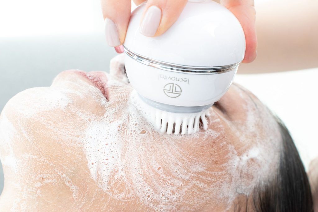 A woman cleansing her face with a handheld electric cleansing brush