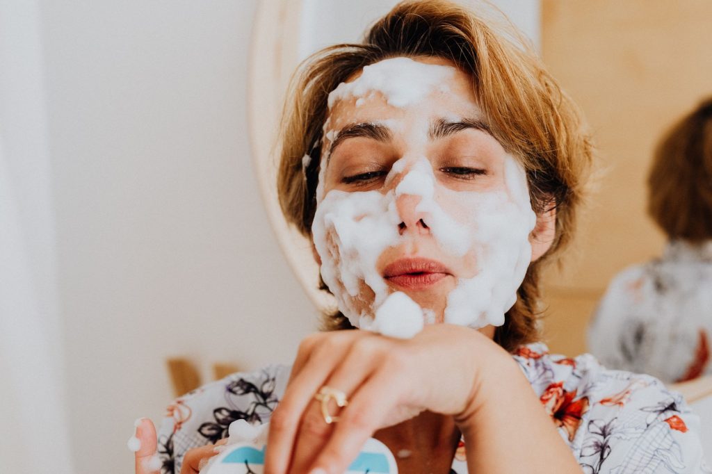A woman rinsing cleanser from her face at a bathroom basin