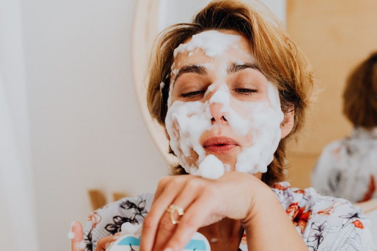 A woman rinsing cleanser from her face at a bathroom basin