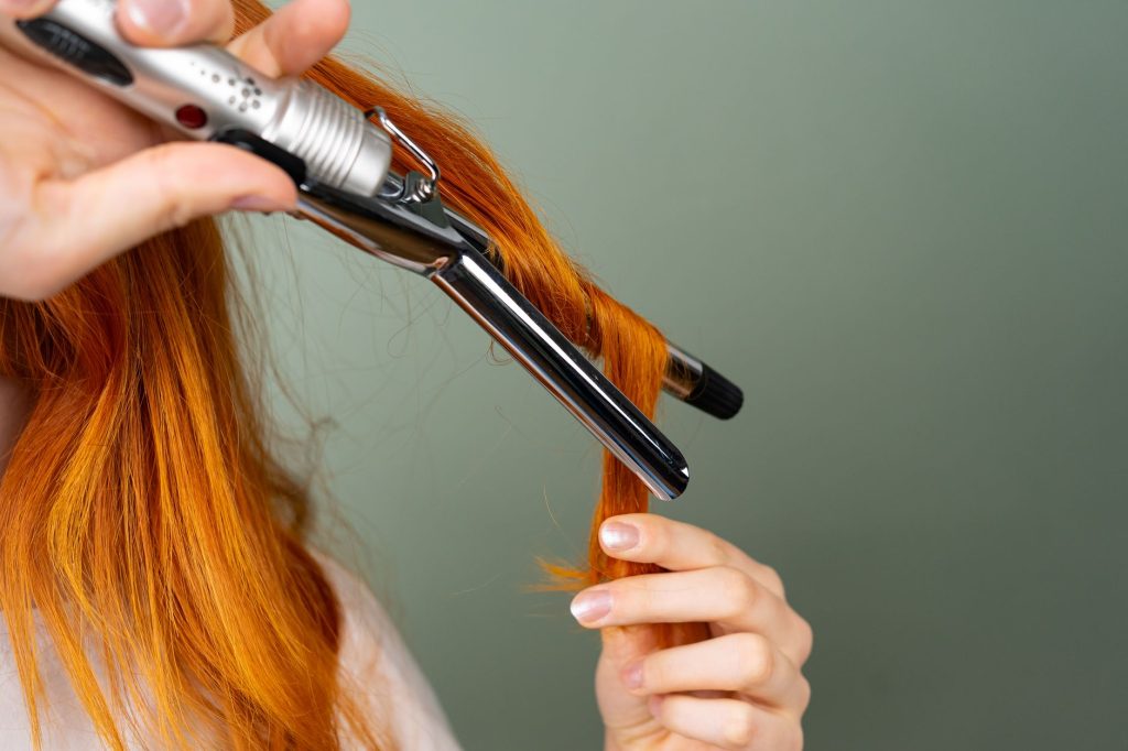 A section of red hair being curled with a heated styling iron