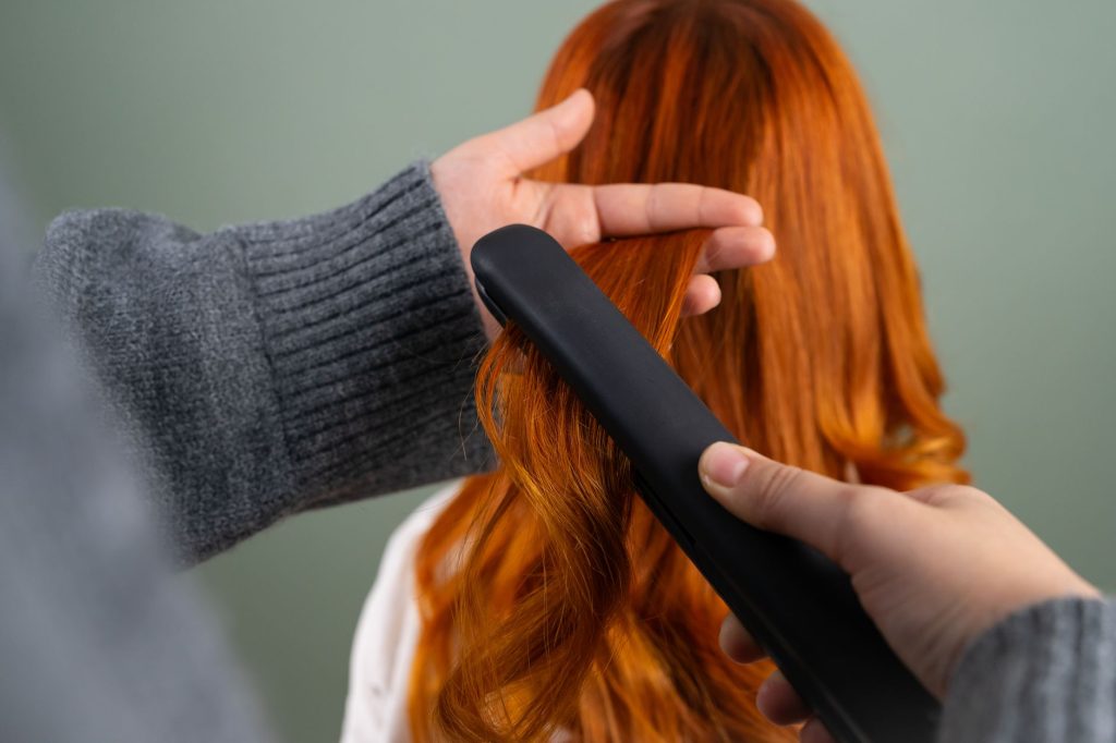 Hands drawing a flat iron through a section of long red hair