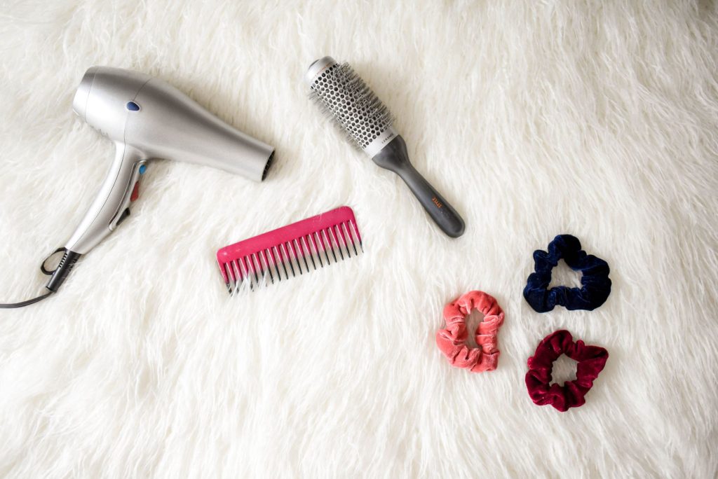 A flat lay of hairstyling tools: hairdryer, brush, comb and scissors