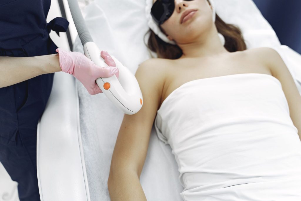 A practitioner passing a light-based hair removal handpiece over a client’s underarm