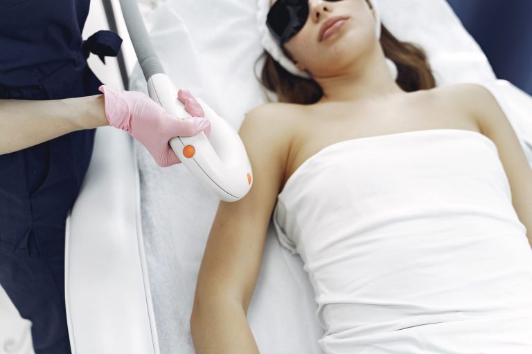A practitioner passing a light-based hair removal handpiece over a client’s underarm