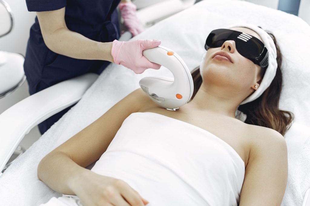 A practitioner in gloves guiding a light-based hair removal handpiece across skin
