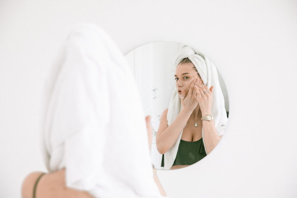 A woman applying face cream at a bathroom mirror