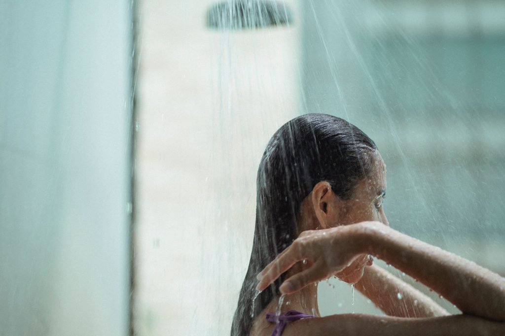 A woman standing under running water in a shower, eyes closed